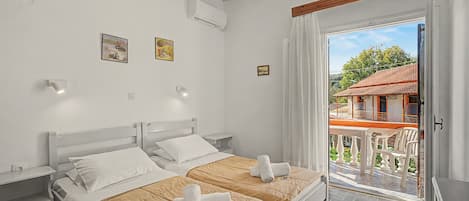 Une chambre d’hôtel avec deux lits, un balcon donnant sur un immeuble et une porte menant à l’extérieur.