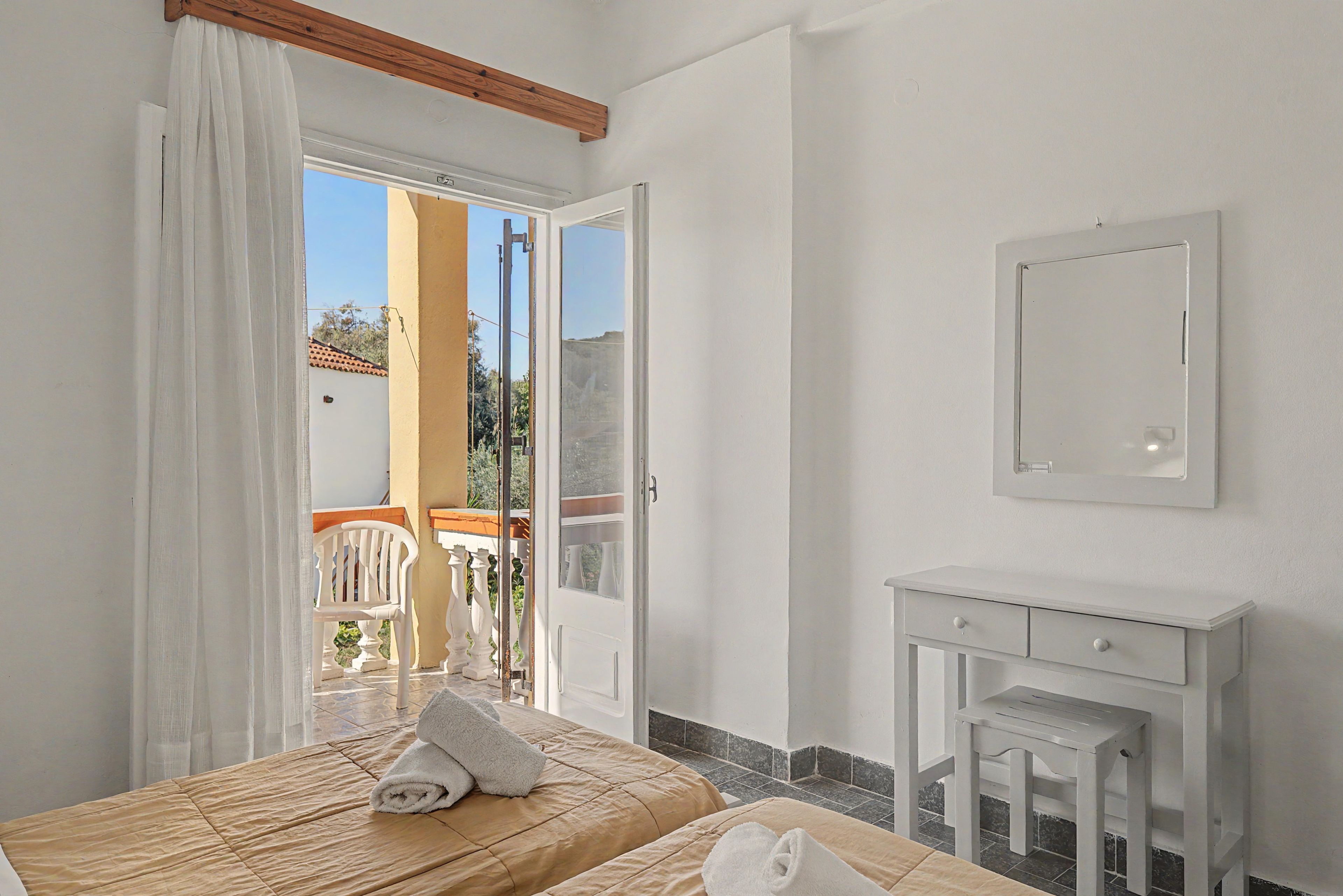 A hotel room with a bed, a bedside table, a mirror, and a balcony with a chair.