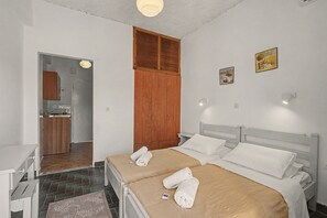 Une chambre avec deux lits, une armoire en bois, un petit coin cuisine et une salle de bain.