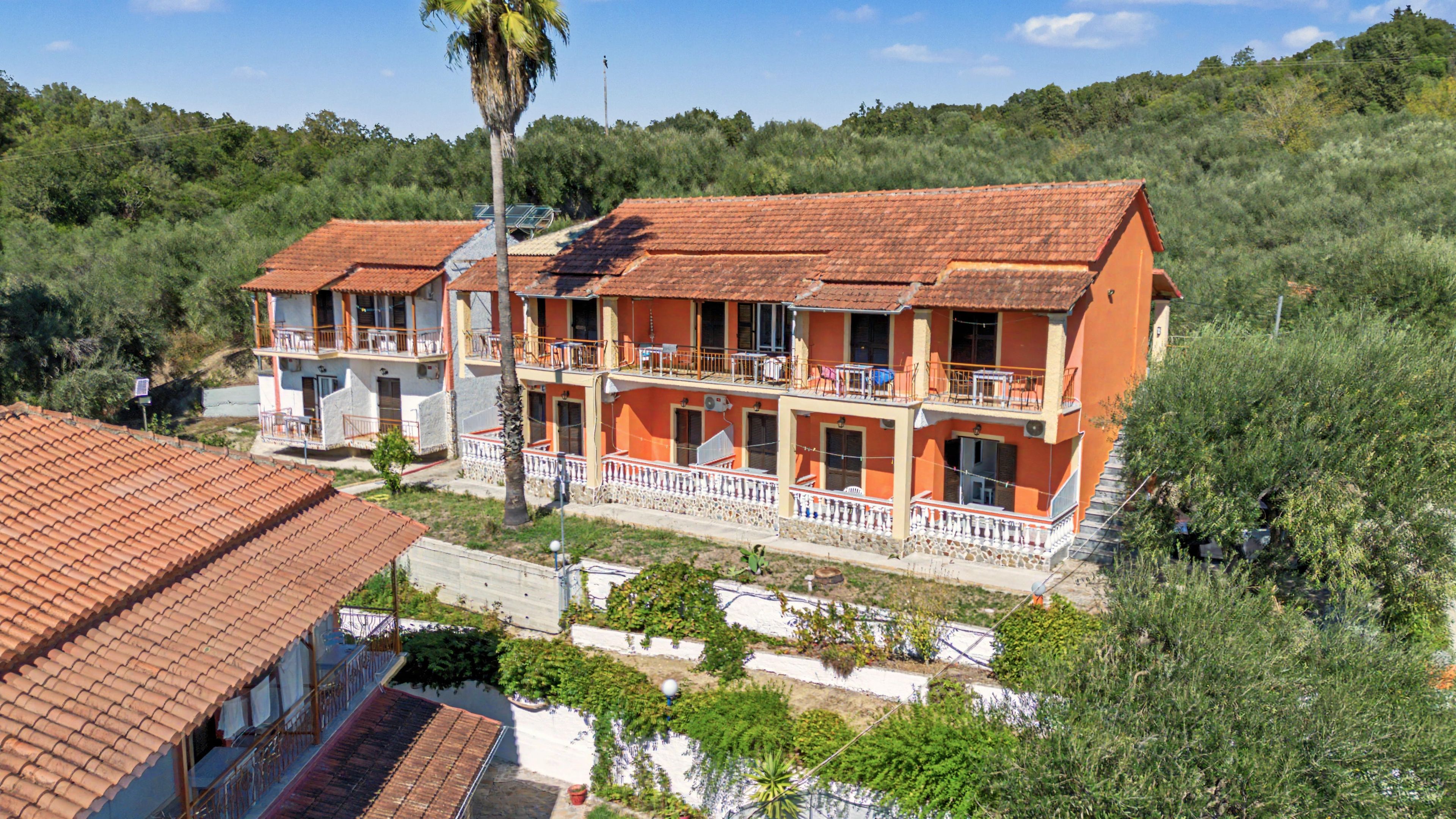 A two-story building with a red-tiled roof, balconies, and a surrounding landscape.