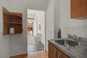 A kitchen with a marble backsplash, wooden cabinets, a stainless steel sink, and a view into a dining area. - Studio Apartment 'Maltas 6' with Shared Terrace, Wi-Fi and Air Conditioning (Corfu)