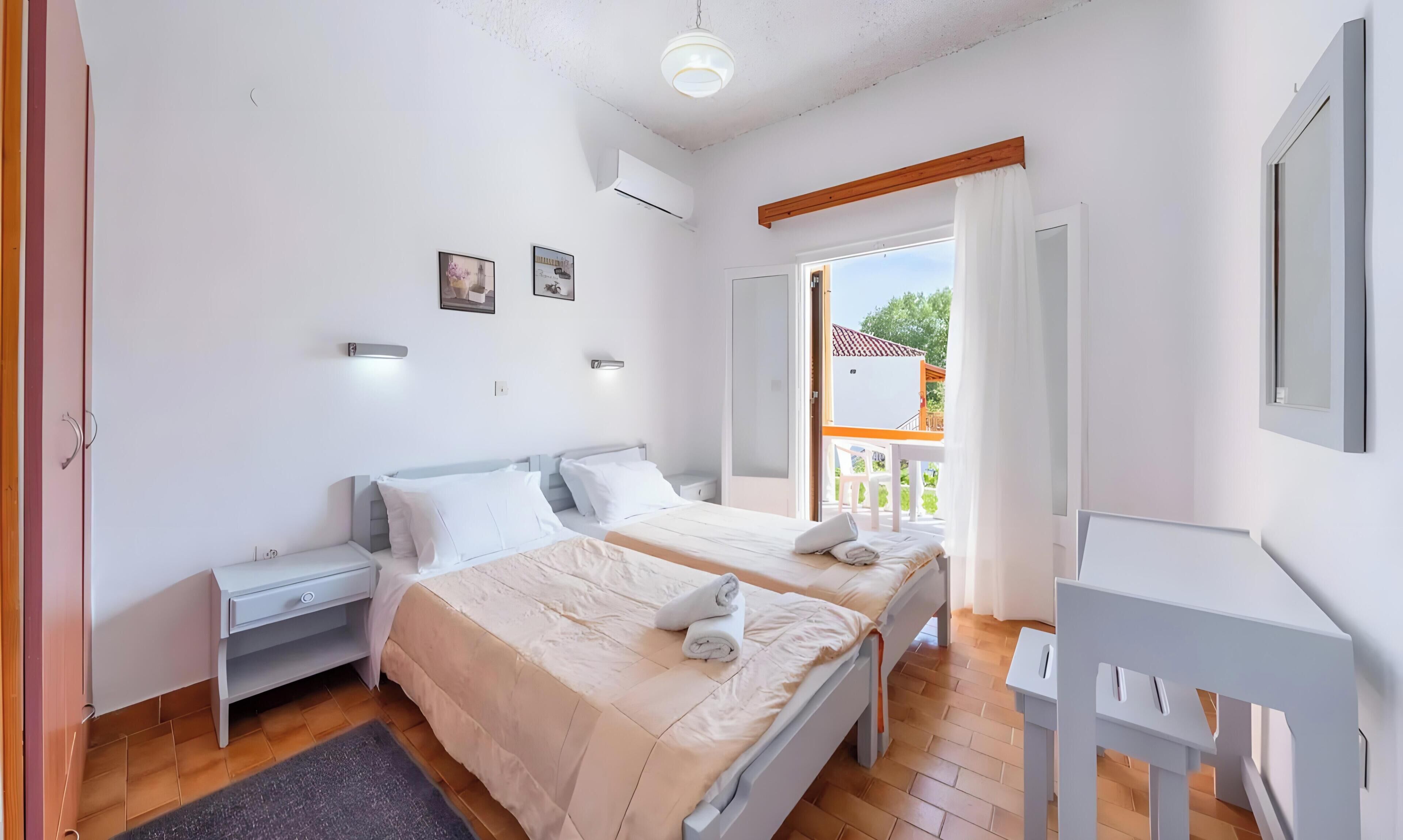 Une chambre avec deux lits, un bureau, une chaise et un balcon avec vue.