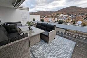 A rooftop terrace with outdoor furniture, a patterned floor, and a view of a town and hills in the background. - Bergliebe 13 - Modern vacation apartment with roof terrace & mountain views (Bad Harzburg)
