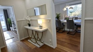 A modern interior with a wooden floor, a white console table with a lamp, a mirror, and a dining area with chairs and a table. - Bergliebe 13 - Modern vacation apartment with roof terrace & mountain views (Bad Harzburg)