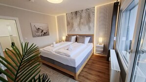 A modern bedroom with a large bed, a wall-mounted artwork, and a large window. - Bergliebe 13 - Modern vacation apartment with roof terrace & mountain views (Bad Harzburg)