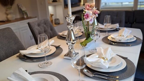 A dining table set with white plates, silverware, and glasses, accompanied by a candle and flowers. - Bergliebe 13 - Modern vacation apartment with roof terrace & mountain views (Bad Harzburg)