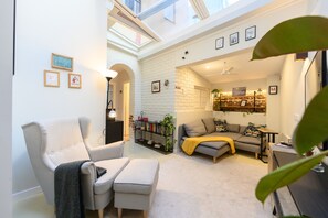 A spacious living area with a high ceiling, a white brick wall, a grey sofa, a white armchair, and a bookshelf with plants. - M (OLM102BA) Spacious and bright apartment for 2 bedrooms (Madrid)