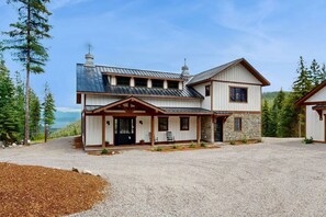 A two-story house with a stone exterior, a metal roof, and a gravel driveway.