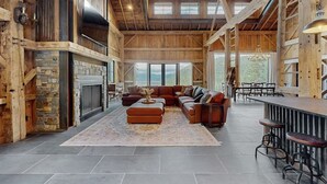 A spacious living area with a stone fireplace, leather sofas, and a bar area with stools. - Flathead Lake Barn House w/Lake & Mountain Views (Lakeside)