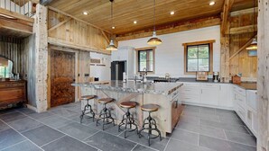 A spacious kitchen with a large island, bar stools, and wooden accents. - Flathead Lake Barn House w/Lake & Mountain Views (Lakeside)