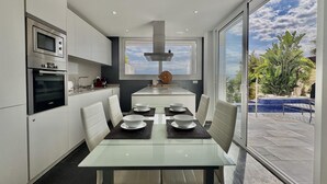 A modern kitchen with a dining area, large windows, and a view of a swimming pool. - Villa Sol in Canyelles with private pool and Wi-Fi (Roses)
