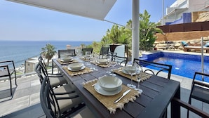 An outdoor dining area with a view of the sea, equipped with tables, chairs, and a pool. - Villa Sol in Canyelles with private pool and Wi-Fi (Roses)