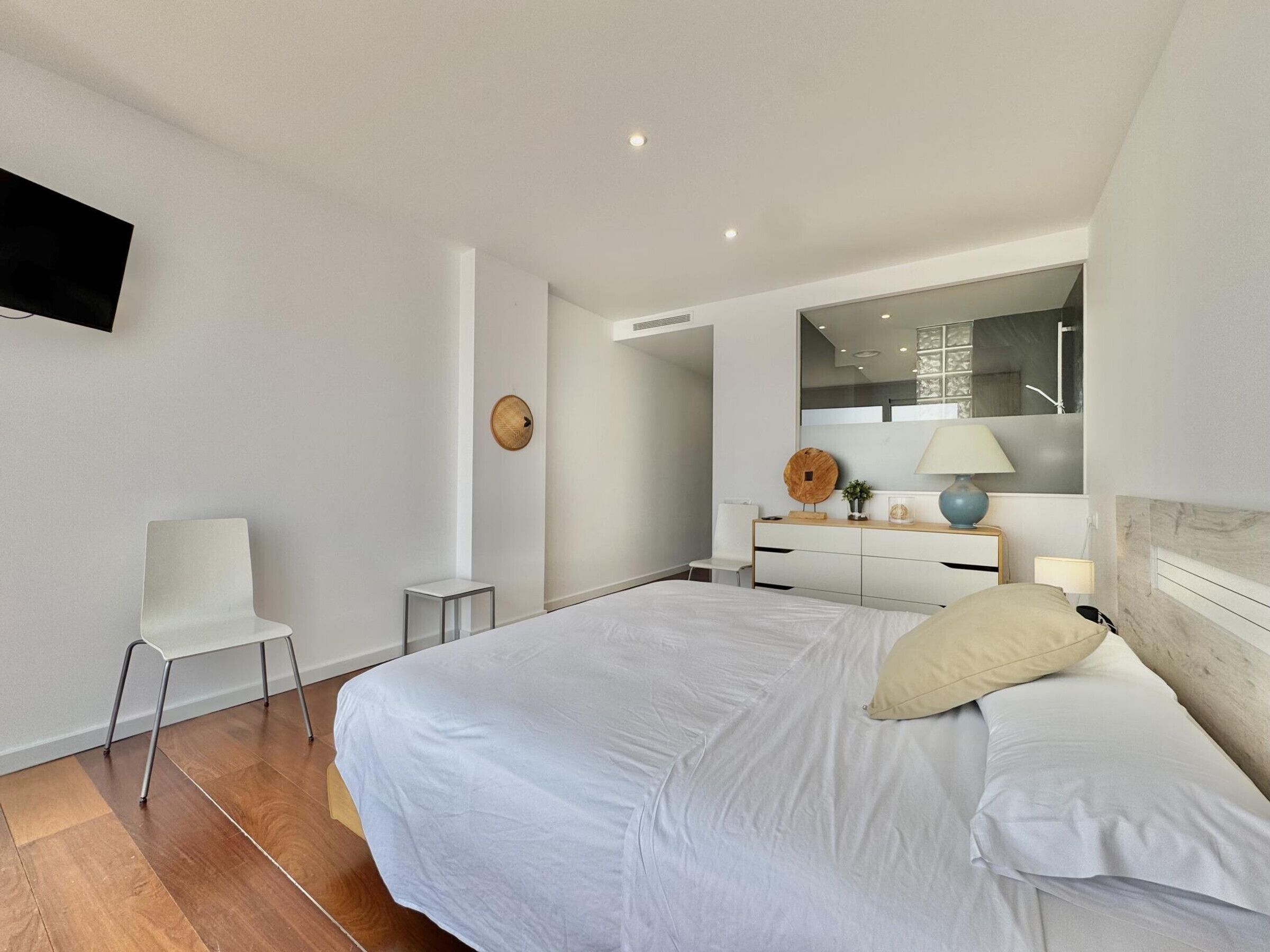 Une chambre moderne avec un grand lit, un bureau, une chaise et un téléviseur fixé au mur.