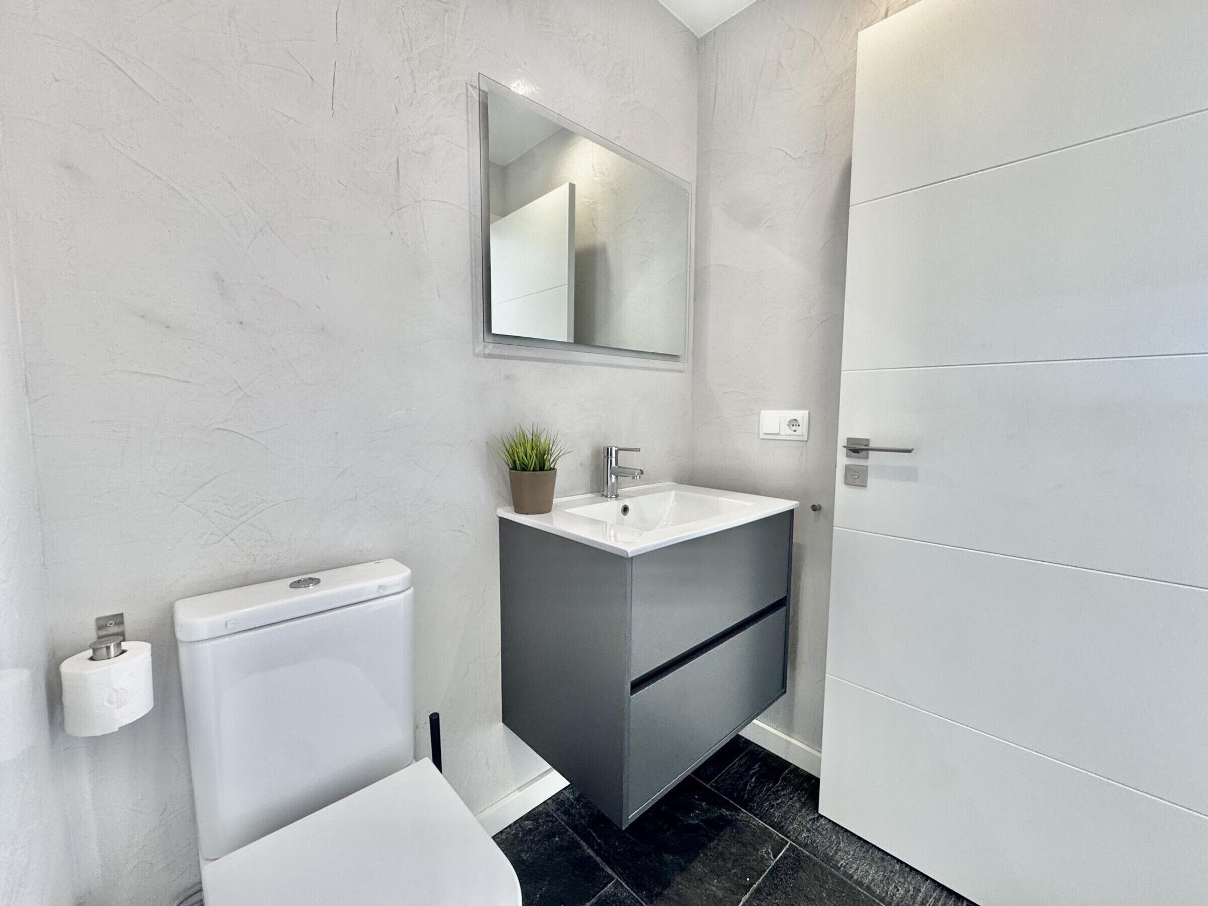 A modern bathroom with a white toilet, a sink with a mirror above it, and a cabinet.
