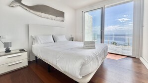 A modern bedroom with a large bed, a bedside table with a lamp, and a view of the ocean through a sliding glass door. - Villa Sol in Canyelles with private pool and Wi-Fi (Roses)