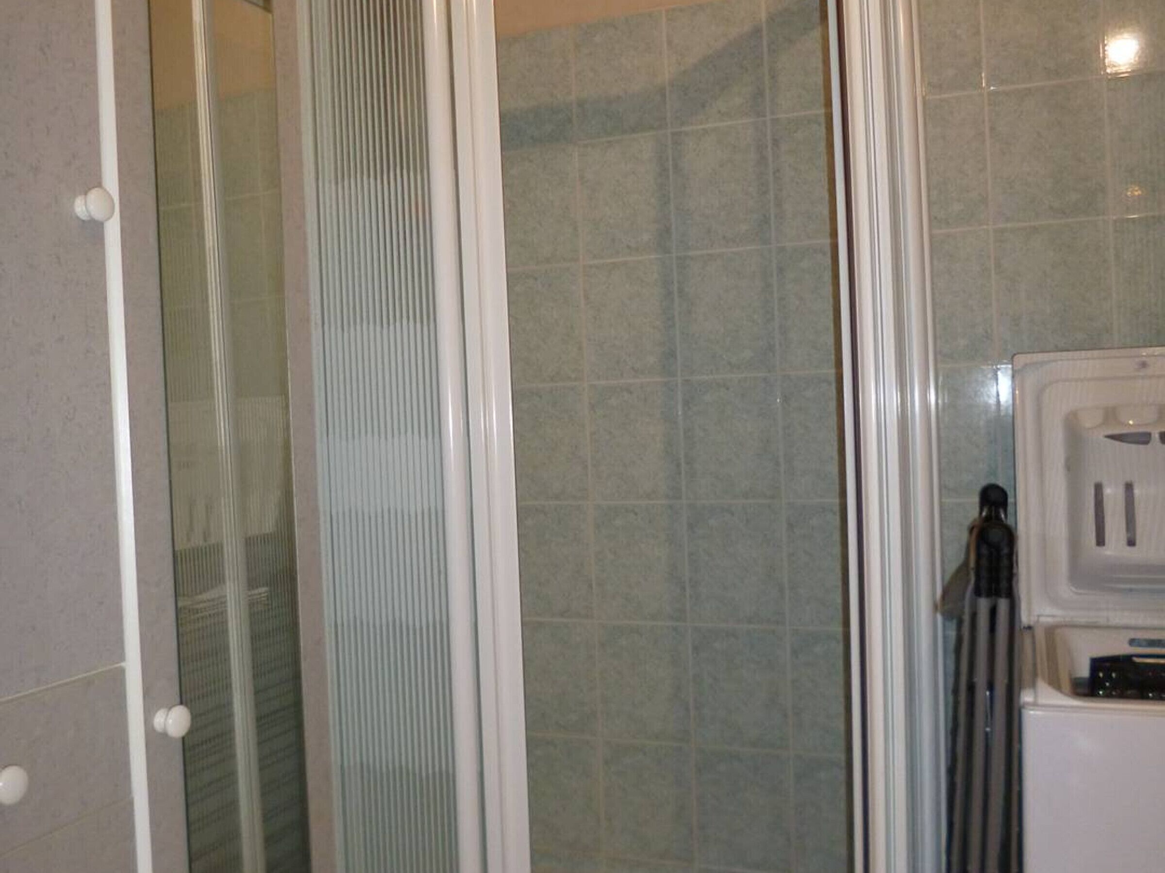Un baño con cabina de ducha de vidrio, paredes con azulejos y un lavamanos blanco con grifo.