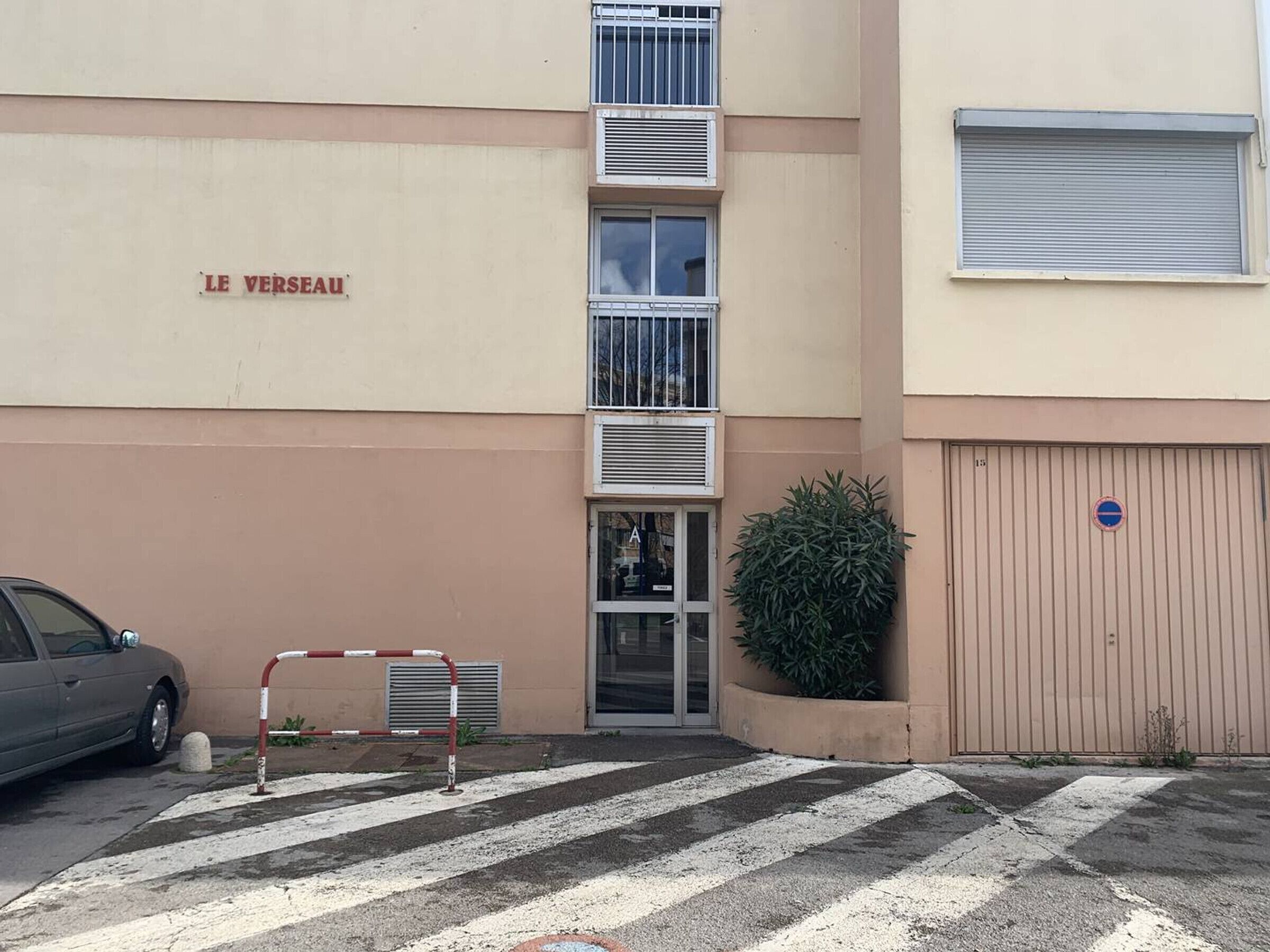 Un edificio con un letrero que dice "LE VERSEAU" y una entrada protegida por una reja.