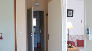 A narrow hallway leading to a kitchen and a living area with a sofa and a lamp. - Charming T2 near Thau Lagoon - 2 guests (Balaruc-les-Bains)
