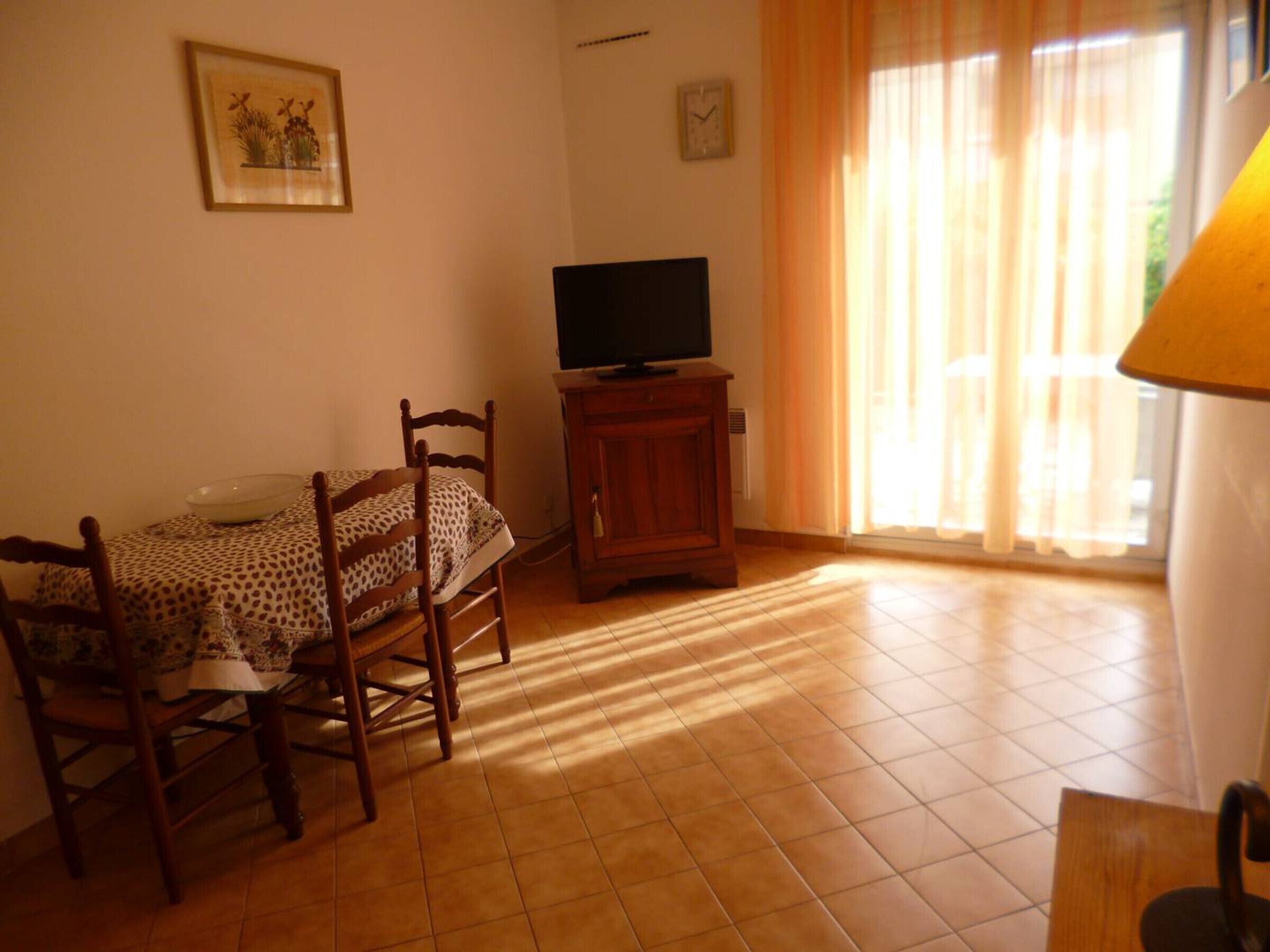 Un comedor con una mesa y sillas, un televisor sobre un mueble bajo y una ventana con cortinas.