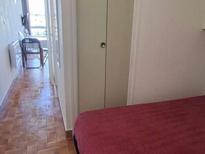 A hotel room with a tiled floor, a bed with a red cover, a wardrobe, and a chair near a window. - Cozy studio, pets allowed - 2 guests (Balaruc-les-Bains)