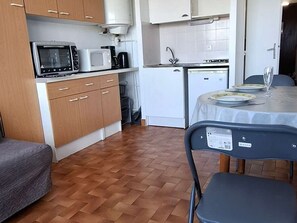 A compact kitchen with a microwave, coffee maker, and a sink. There is a dining table with plates and a glass. - Cozy studio, pets allowed - 2 guests (Balaruc-les-Bains)