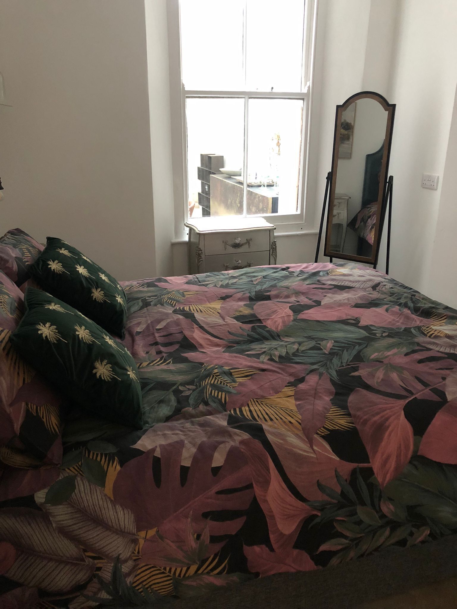Quarto com cama, cômoda, janela e espelho.
