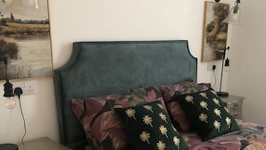 En seng med blomstret dyne, to puder, et natbord med skuffer og to vægmonterede lamper.