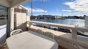 A balcony with a table and chairs, overlooking a marina with boats and buildings. - Marina Saphirre-Port Ulysse -P2 (Le Grau-du-Roi)