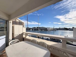 Ein Balkon mit Tisch und Stühlen, der auf einen Yachthafen mit Booten und Gebäuden blickt.