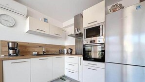 Eine moderne Küche mit weißen Schränken, einem Edelstahlkühlschrank, einem eingebauten Backofen und einer Kaffeemaschine.