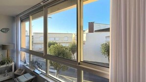 Ein Zimmer mit einem großen Fenster, einem Nachttisch, einem Stuhl und einer Pflanze.