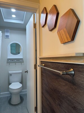 A bathroom with a toilet, a mirror, and wooden wall decor. - Sea Shells II_Beach Views From Bed (Myrtle Beach)