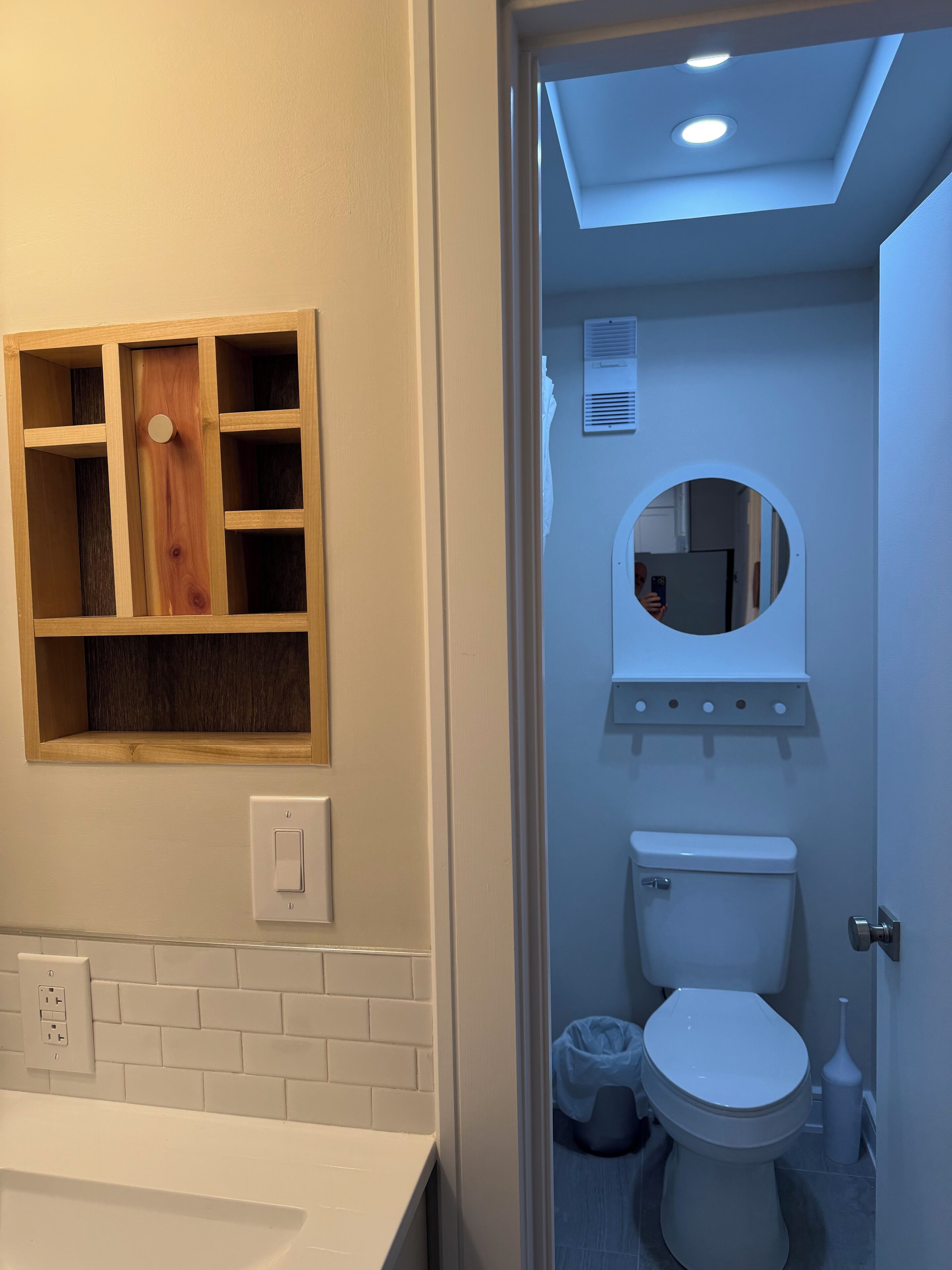 Une salle de bain comprenant des toilettes, un lavabo, un miroir et une étagère en bois.