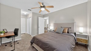 Ein Schlafzimmer mit einem großen Bett, einem Schreibtisch mit Stuhl, einem Deckenventilator und einem Nachttisch mit Lampe.