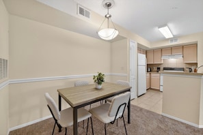 A compact kitchen with a dining area, featuring a wooden table, white chairs, and a potted plant. - Modern 2BR Stay in Prime Location (Winter Springs)