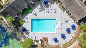 An aerial view of a swimming pool area with lounge chairs and umbrellas, surrounded by greenery and buildings. - Modern 2BR Stay in Prime Location (Winter Springs)