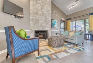 Un hall d’entrée avec une cheminée en pierre, un fauteuil bleu à motifs, un canapé gris et un tapis à motifs.