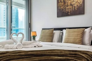 Quarto de hotel com cama, almofadas, uma luminária e vista para edifícios através de uma janela.