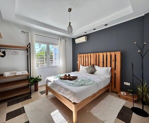A modern bedroom with a wooden bed, a bedside table, a hanging light fixture, and a window with curtains. - Sunny Blue Apartment in la Marsa (La Marsa)