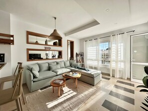 A modern living room with a sectional sofa, a coffee table, and a large window with curtains. - Sunny Blue Apartment in la Marsa (La Marsa)