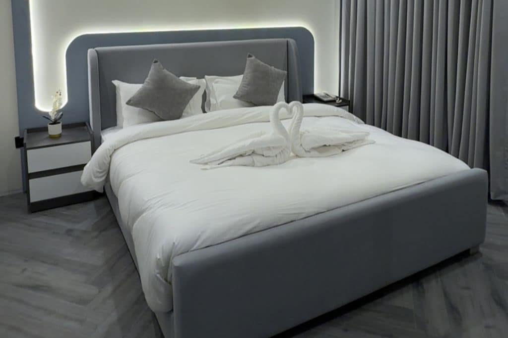 A modern hotel room with a large bed, a nightstand, and a lamp.