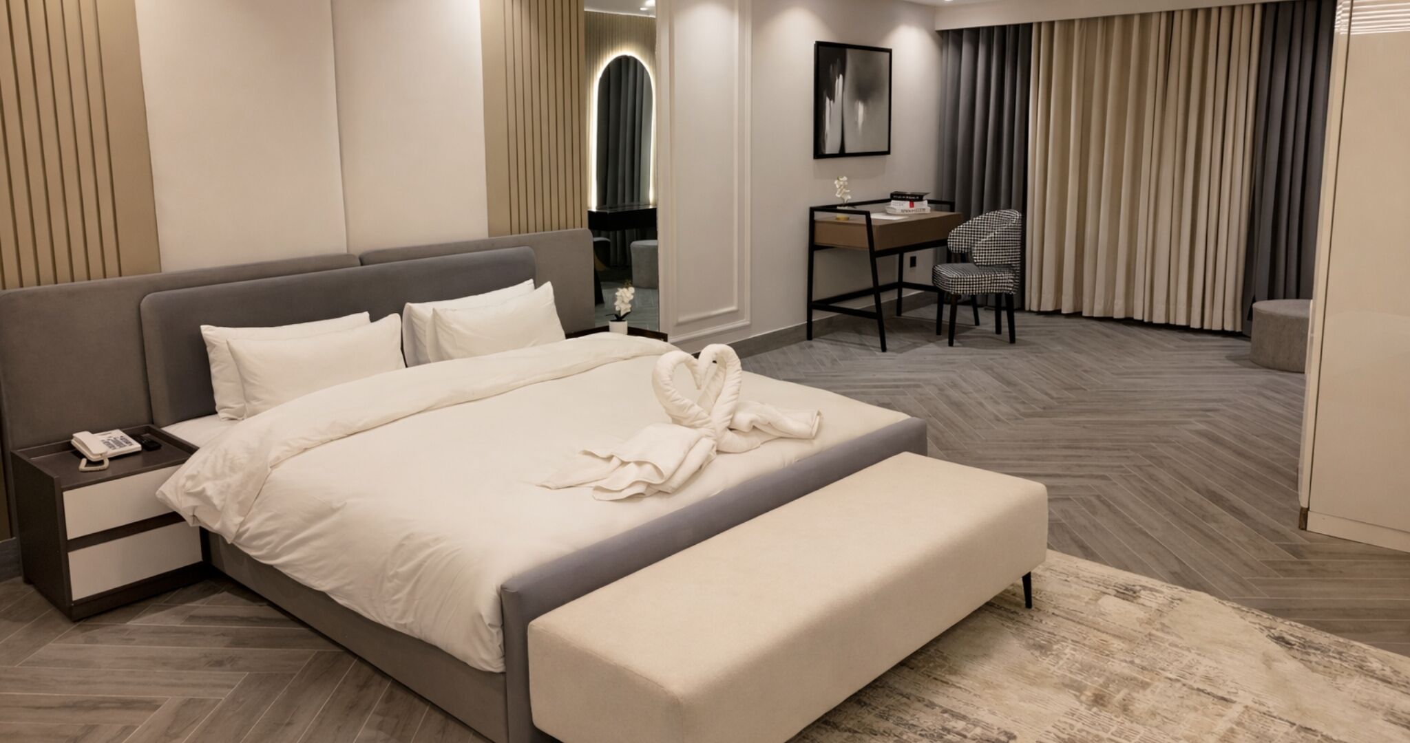 Una habitación de hotel moderna con una cama grande, una mesita de noche con teléfono, un escritorio con silla y un espejo.