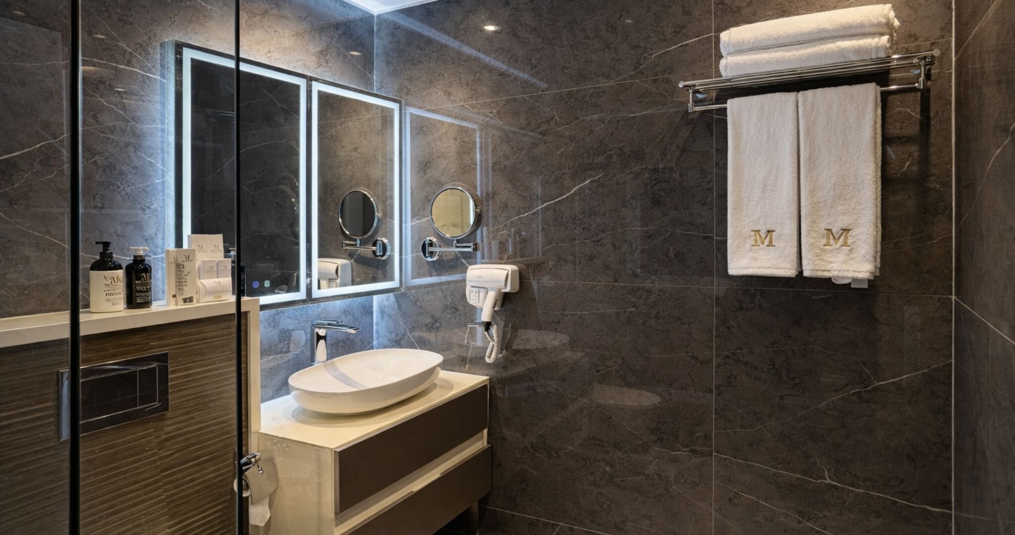 A modern bathroom with a glass shower enclosure, a large mirror, a vanity with a sink, and a towel rack with towels.