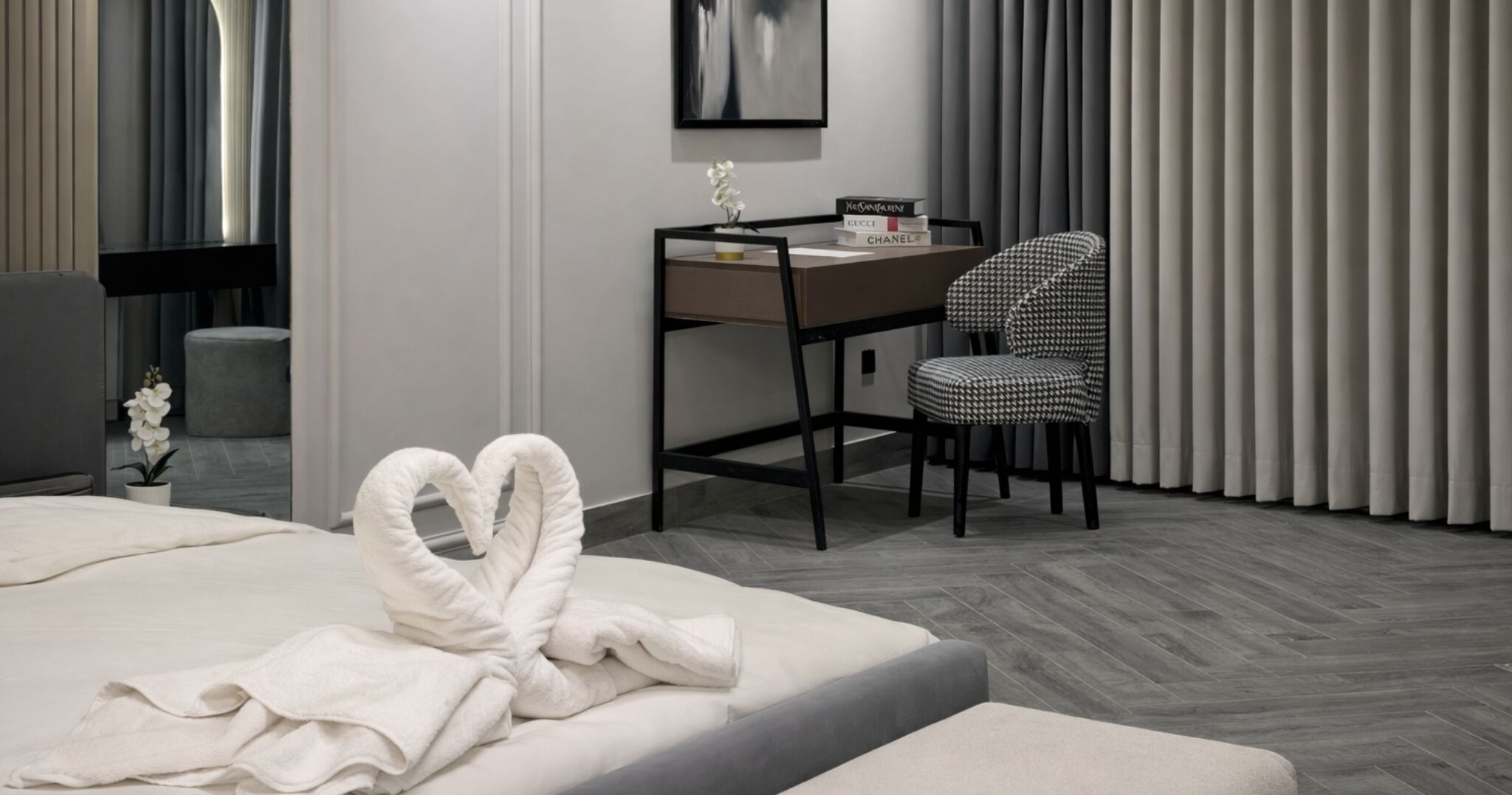 A modern hotel room with a neatly made bed, a desk with a chair, and a large window with curtains.