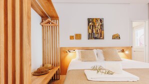 A modern bedroom with a wooden headboard, a bed with white linens, and a small bench with a woven basket. - Laranjal Rive Gauche (Tavira)