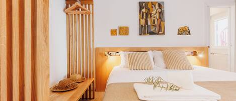 A modern bedroom with a wooden headboard, a bed with white linens, and a small bench with a woven basket.