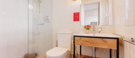 A modern bathroom with a glass shower enclosure, a white toilet, and a wooden vanity with a mirror.