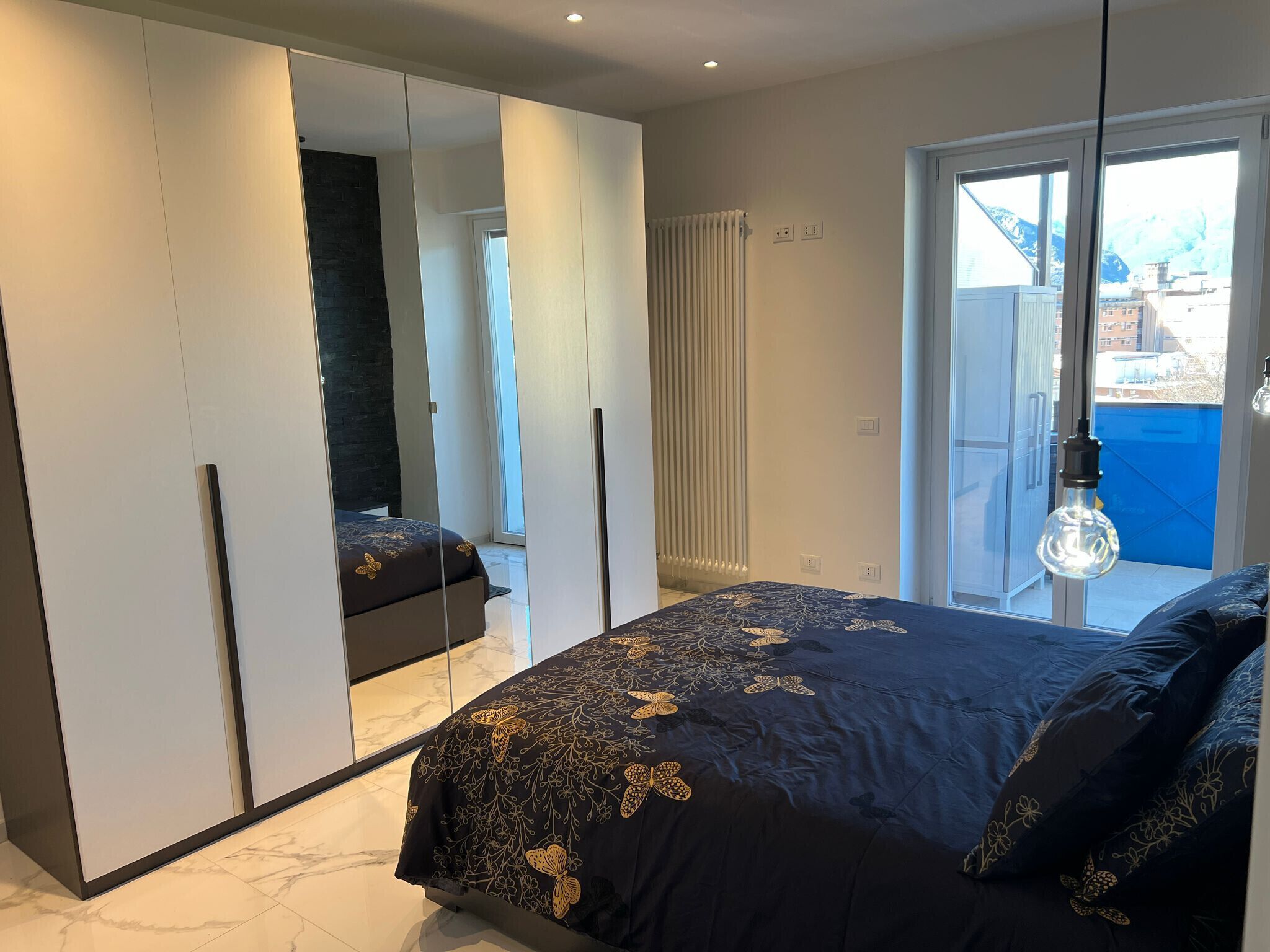 A bedroom with a bed, a large mirror, a radiator, and a view of the outside.