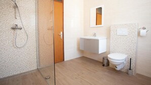 Een moderne badkamer met een douchecabine van glas, een wit wastafelmeubel en een toilet.