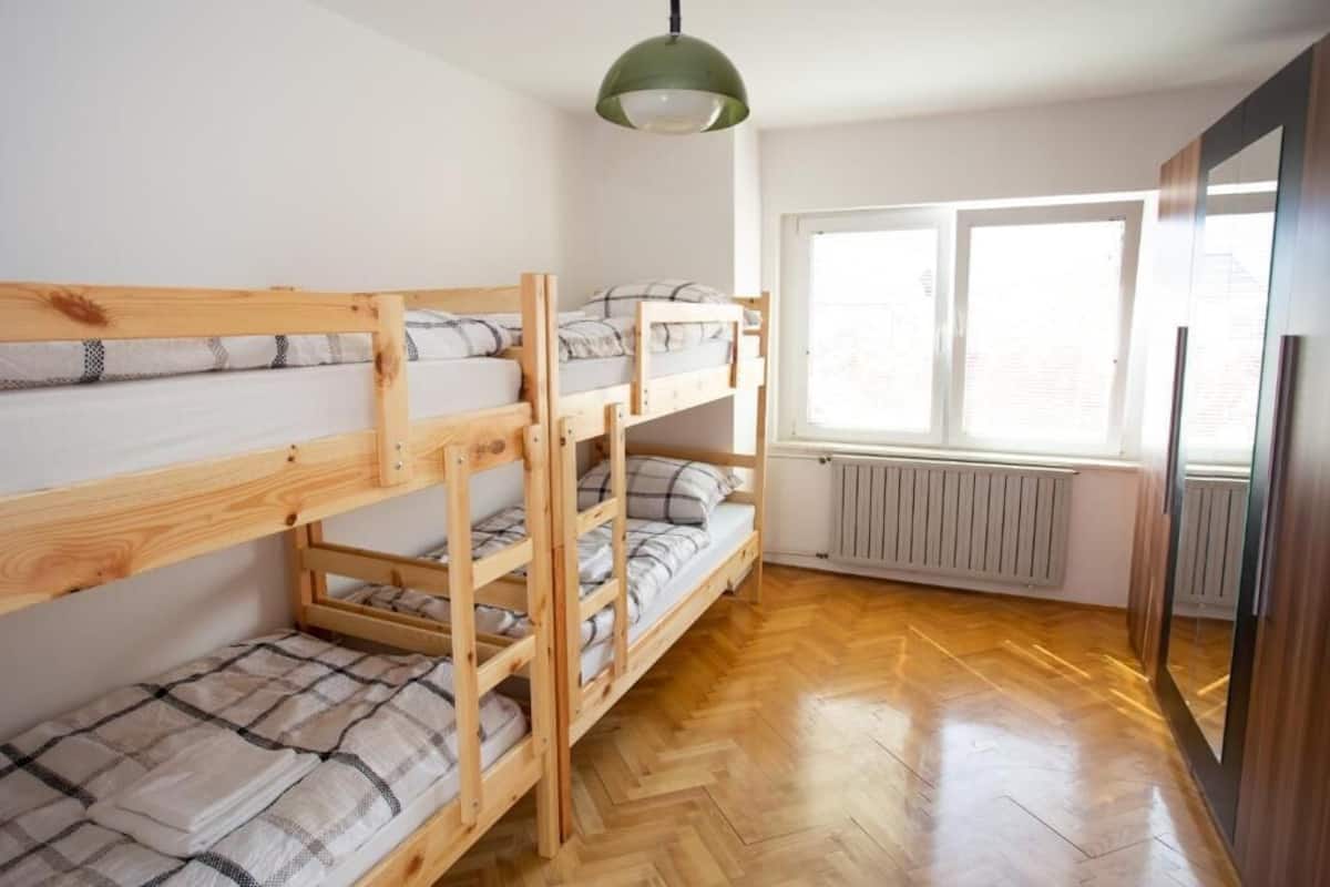 A bunk bed room with a wooden floor, a radiator, and a window with blinds.